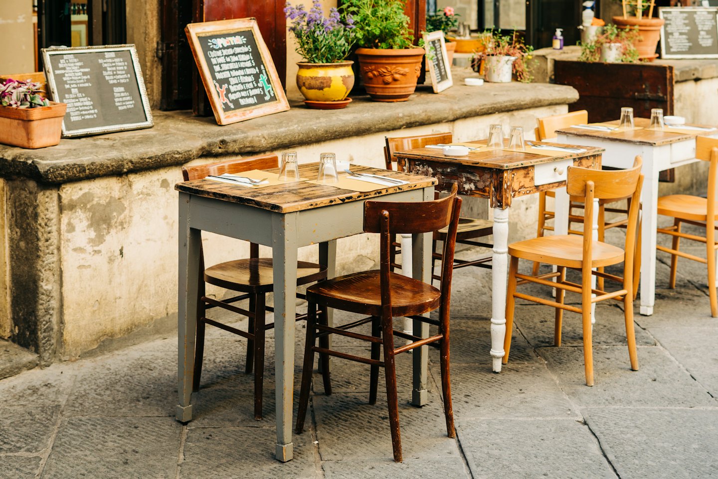 Tavoli e sedie vuoti di un bar all'aperto su una strada di pietra.