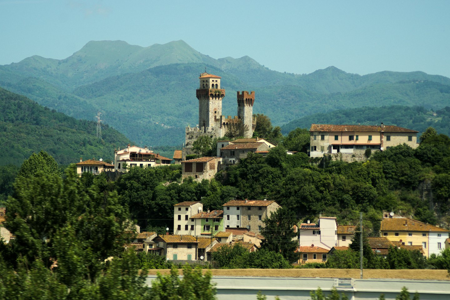 Castello storico in pietra che domina un villaggio con case dai tetti in cotto.