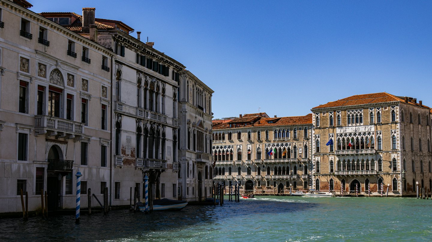 Una piccola barca rossa naviga in un canale veneziano.