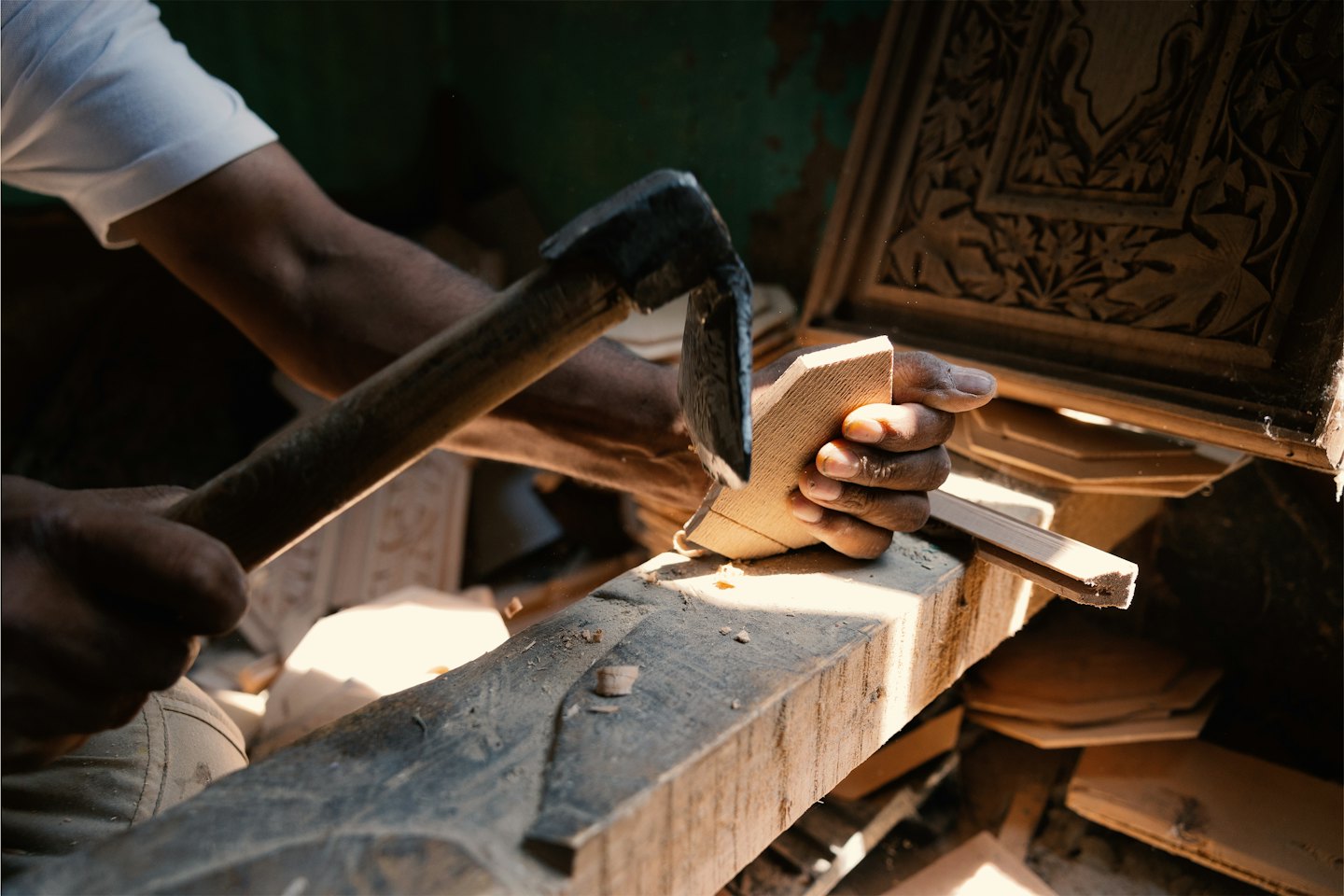 Artigiano che intaglia dettagli intricati in legno chiaro con uno strumento.